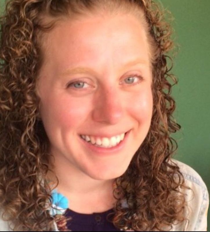 Photo of a White woman smiling with curly reddish-brown hair, wearing a t-shirt.