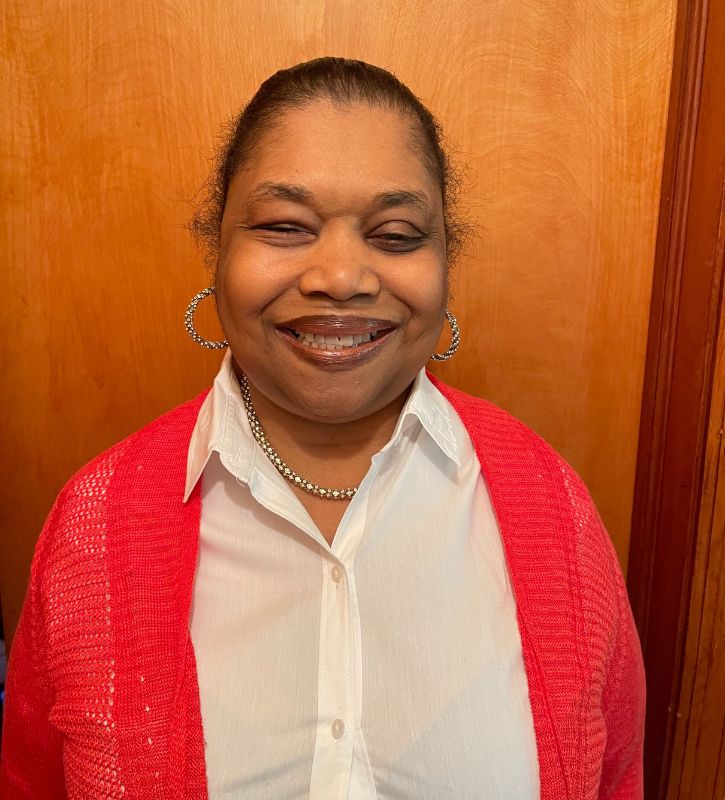 Headshot of Phyllis Hampton, a Black woman wearing gold hoop earrings, a gold necklace, a white button-down shirt, and red sweater.