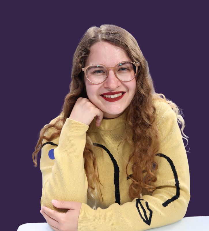 Headshot of Sammie Walker Herrera, a mixed-race advocate with long, curly auburn hair wearing a yellow sweater, red lipstick, and peach-colored glasses.  