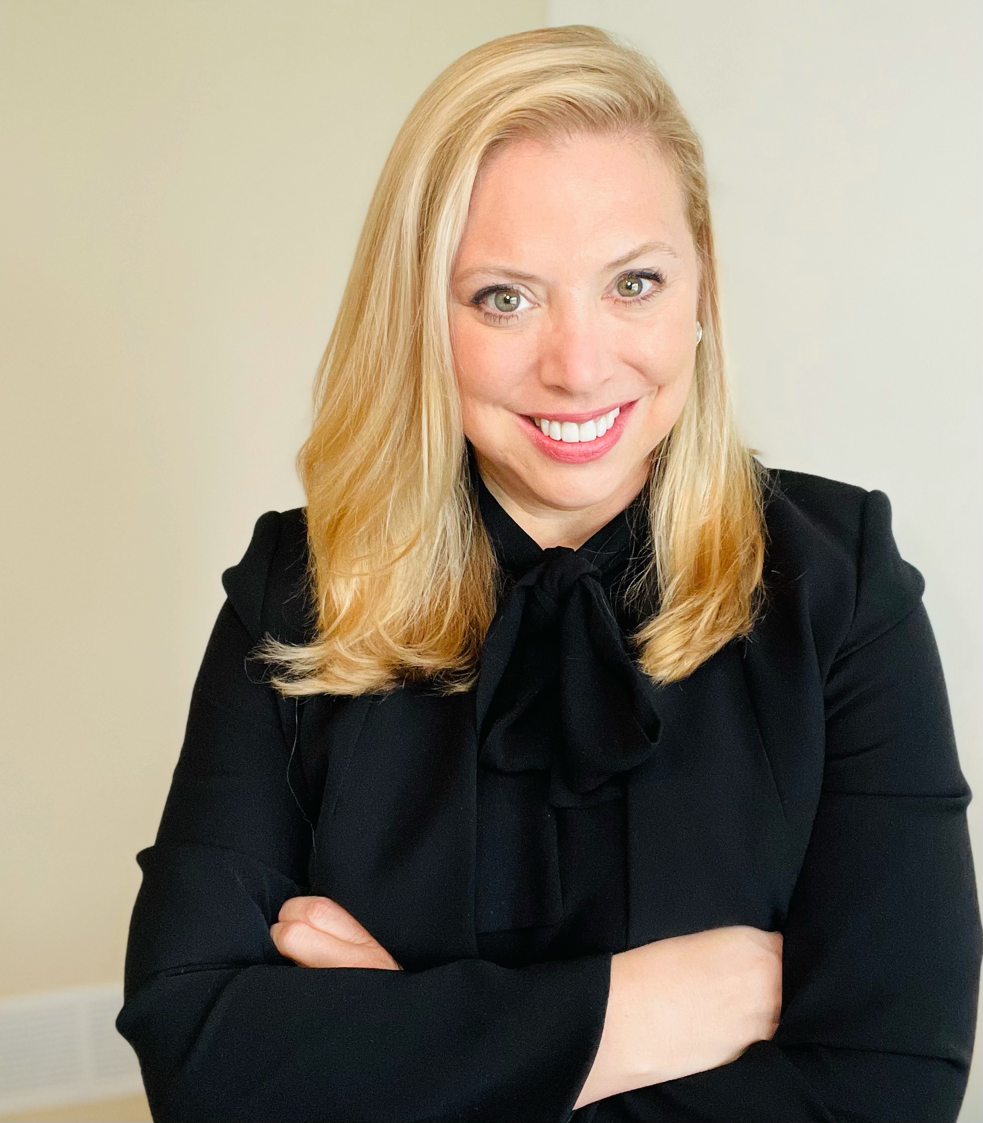 A White woman with Chest length blonde hair. Lisa is smiling with her arms folded wearing a black blazer and black top.