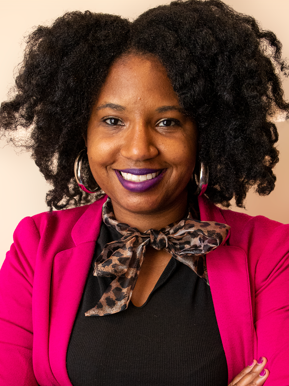 Sydney is smiling wearing a pink blazer, black shirt, and an animal print scarf.
