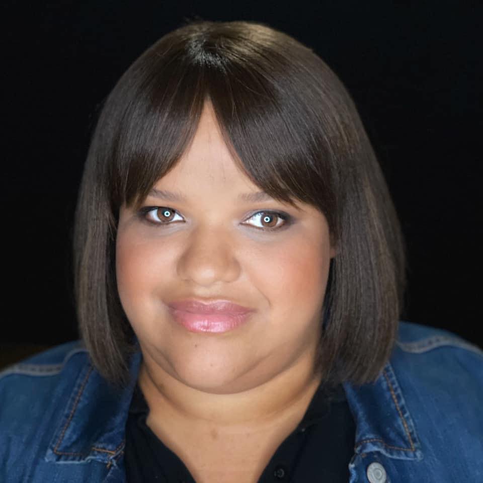 A Black woman with chin length straight black hair and bangs wearing a jean jacket.