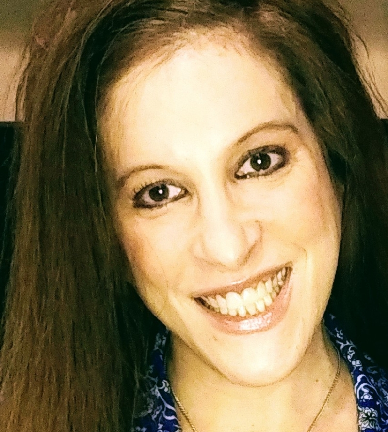 Jinny is smiling. She has long straight brown hair and is wearing eyeliner.