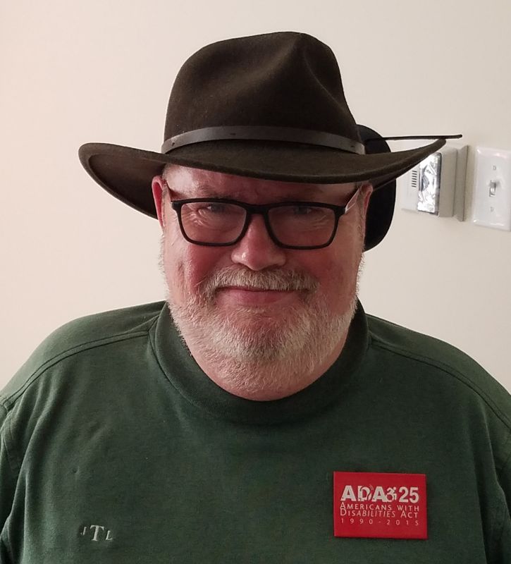 White man with white beard wearing a western style, brimmed hat and glasses.