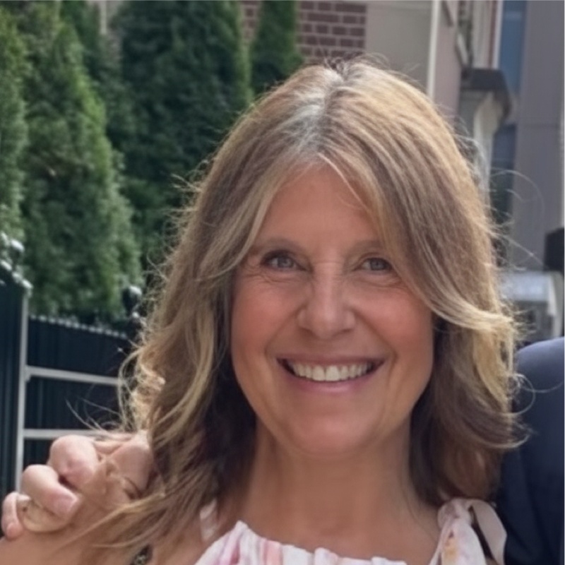 Headshot of Jill Zakon, a white woman with curly blonde hair wearing a pink, orange, and white top.