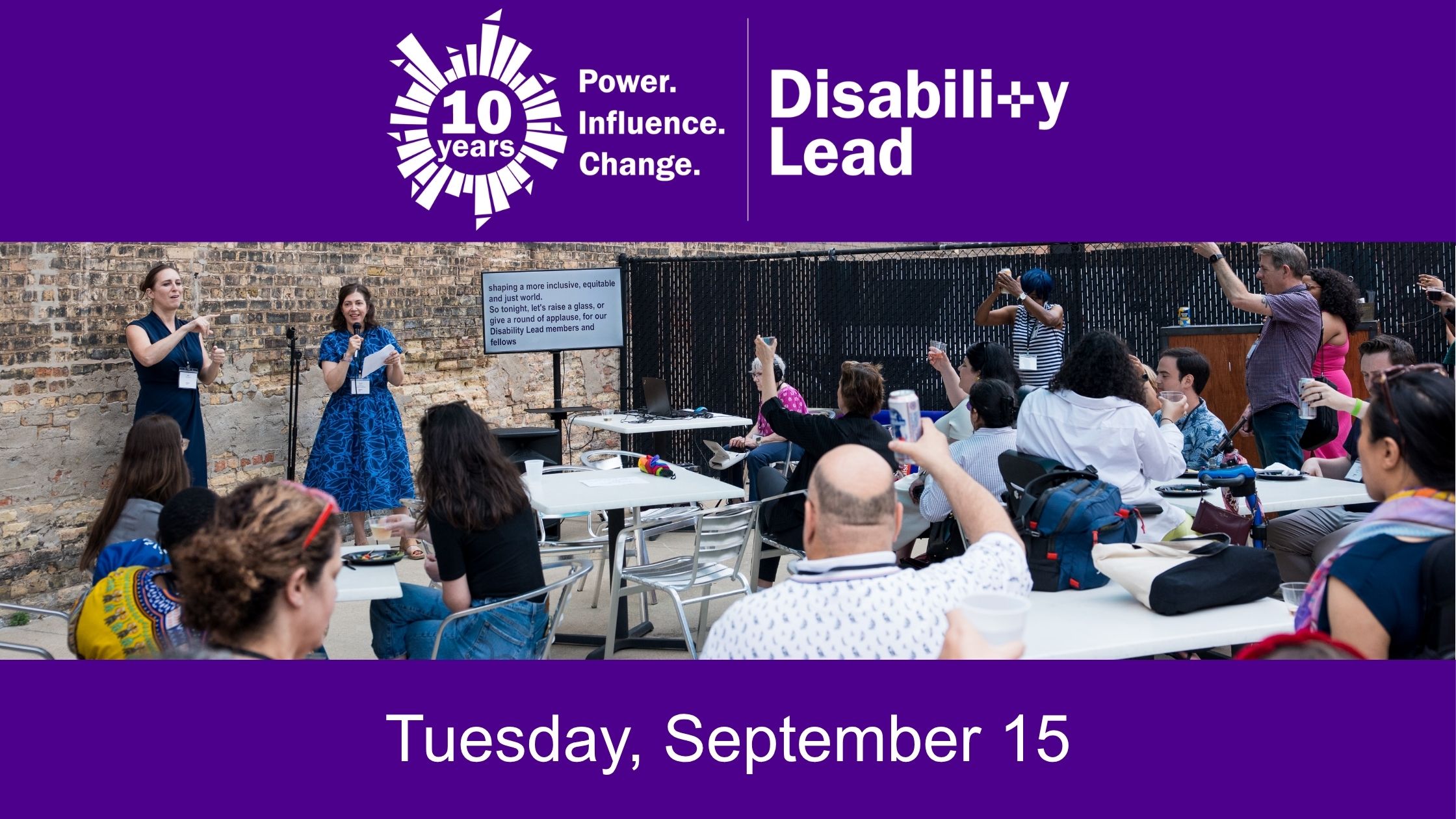 In between 2 purple bars is a photo of an outdoor event with Disability Lead Members of different races, gender expressions, and disabilities are gathered at tabes with their hands raised as prompted by the seaker. Beside the speaker is an ASL interpreter and screen with live captioning.