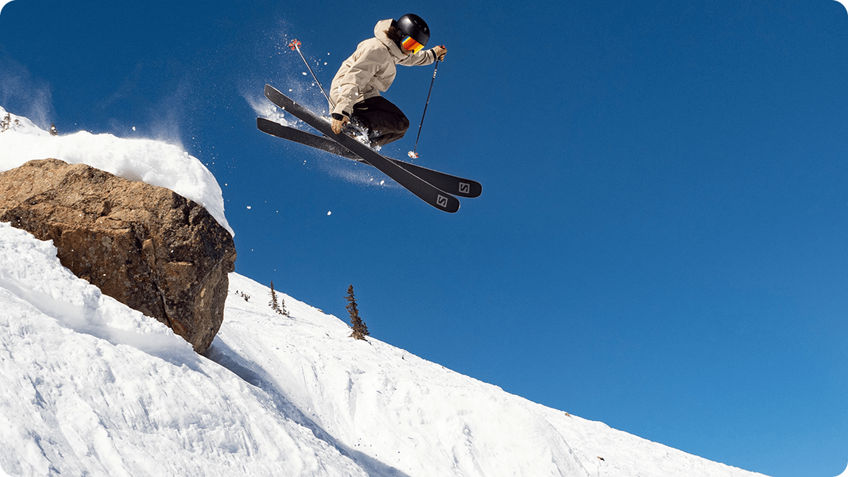 Action shot of a man skiing. He's mid air, after skiing over a large rock.