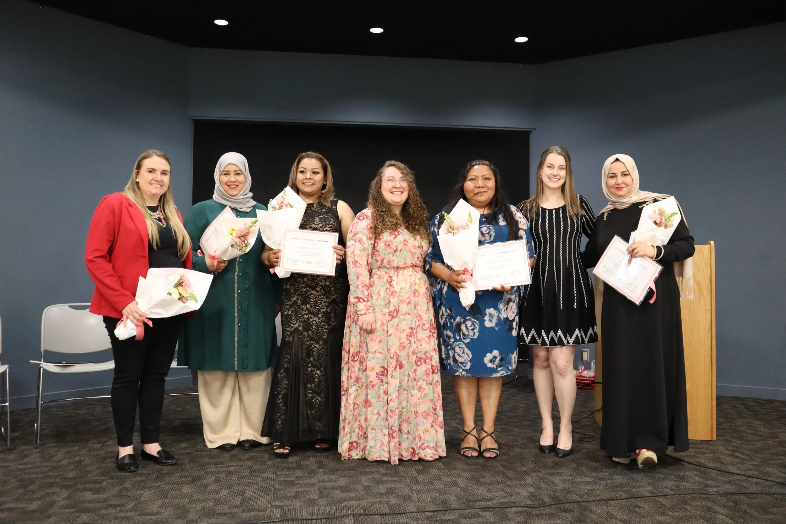 A group of women from the Echo Collective, smiling, holding certificates and a bouquet of flowers.