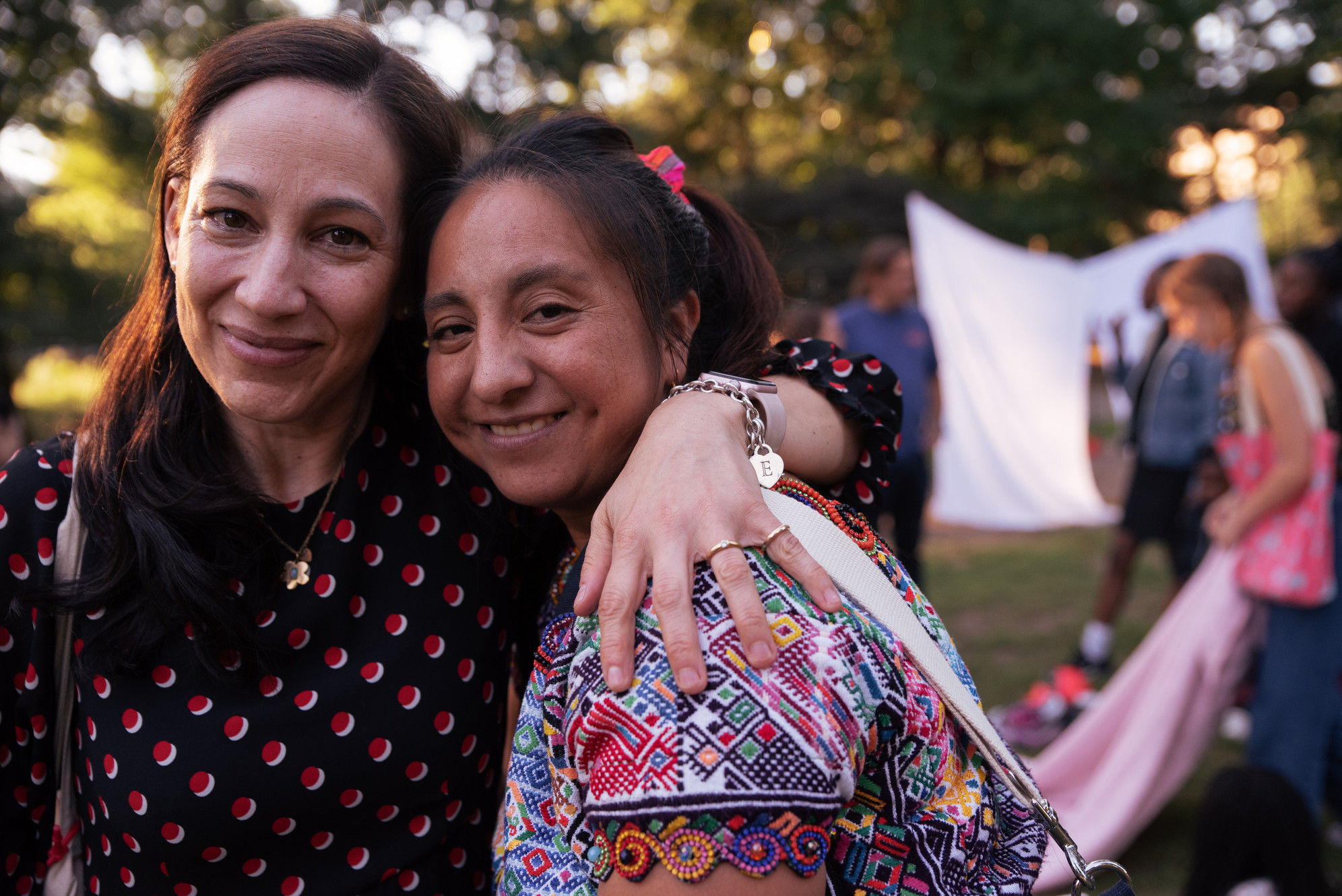 Two women outside, one with her arm around the other's shoulder, smiling at the camera, from the New Neighbors Partnership.