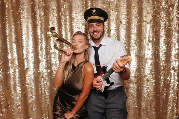 Pareja posando en el fotomatón Selfriends durante una boda en Barcelona, con fondo dorado de lentejuelas, accesorios musicales y un ambiente divertido ideal para animar el evento.