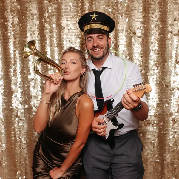 Pareja posando en el fotomatón Selfriends durante una boda en Barcelona, con fondo dorado de lentejuelas, accesorios musicales y un ambiente divertido ideal para animar el evento.