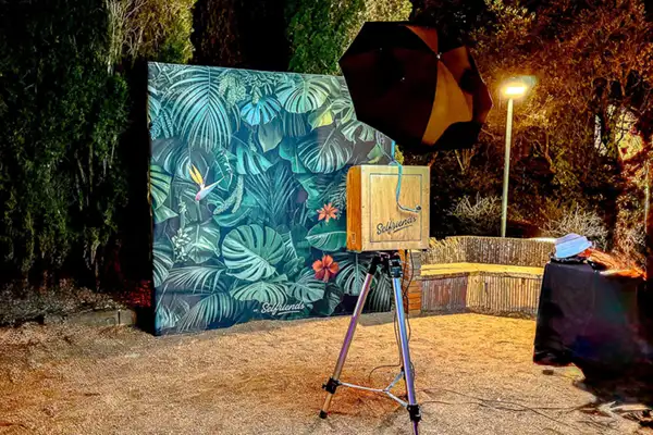 Fotomatón vintage de Selfriends instalado en boda al aire libre en Barcelona, con fondo tropical, iluminación profesional y cámara réflex, ofreciendo fotos de alta calidad y diversión garantizada para los invitados.
