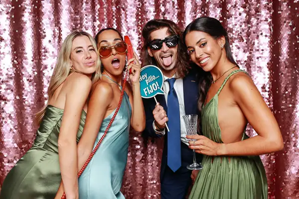 Grupo de invitados disfrutando del fotomatón de bodas en Barcelona con fondo de lentejuelas rosas, accesorios divertidos y copas en mano, durante una celebración capturada por Selfriends Fotomatón.