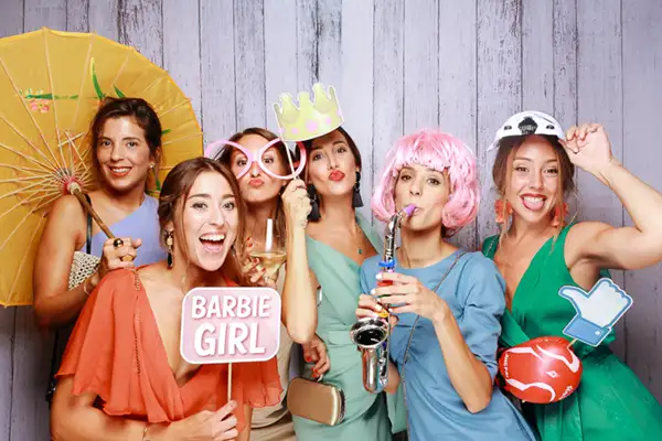 Invitadas disfrutando del fotomatón Selfriends con pelucas y carteles personalizados en un evento.