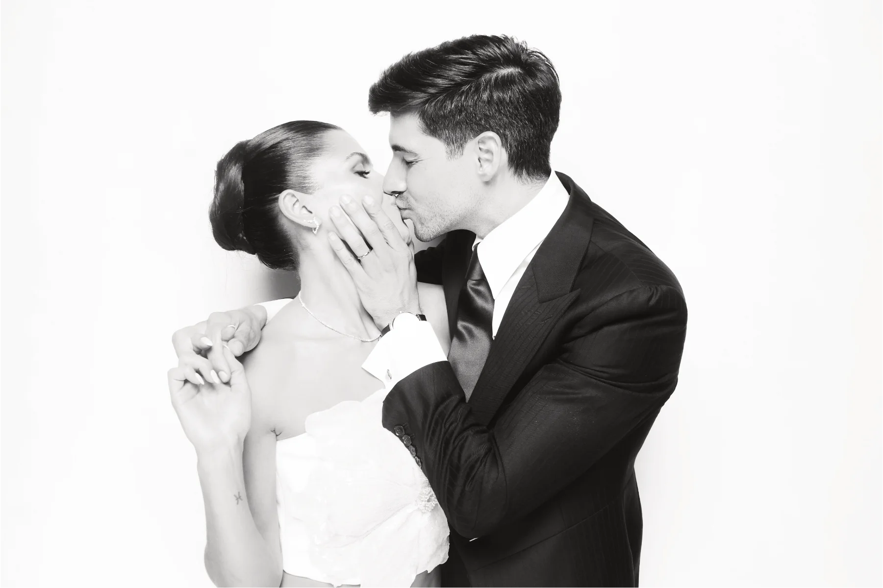 Bride and groom kissing in an elegant black-and-white wedding photo booth portrait.