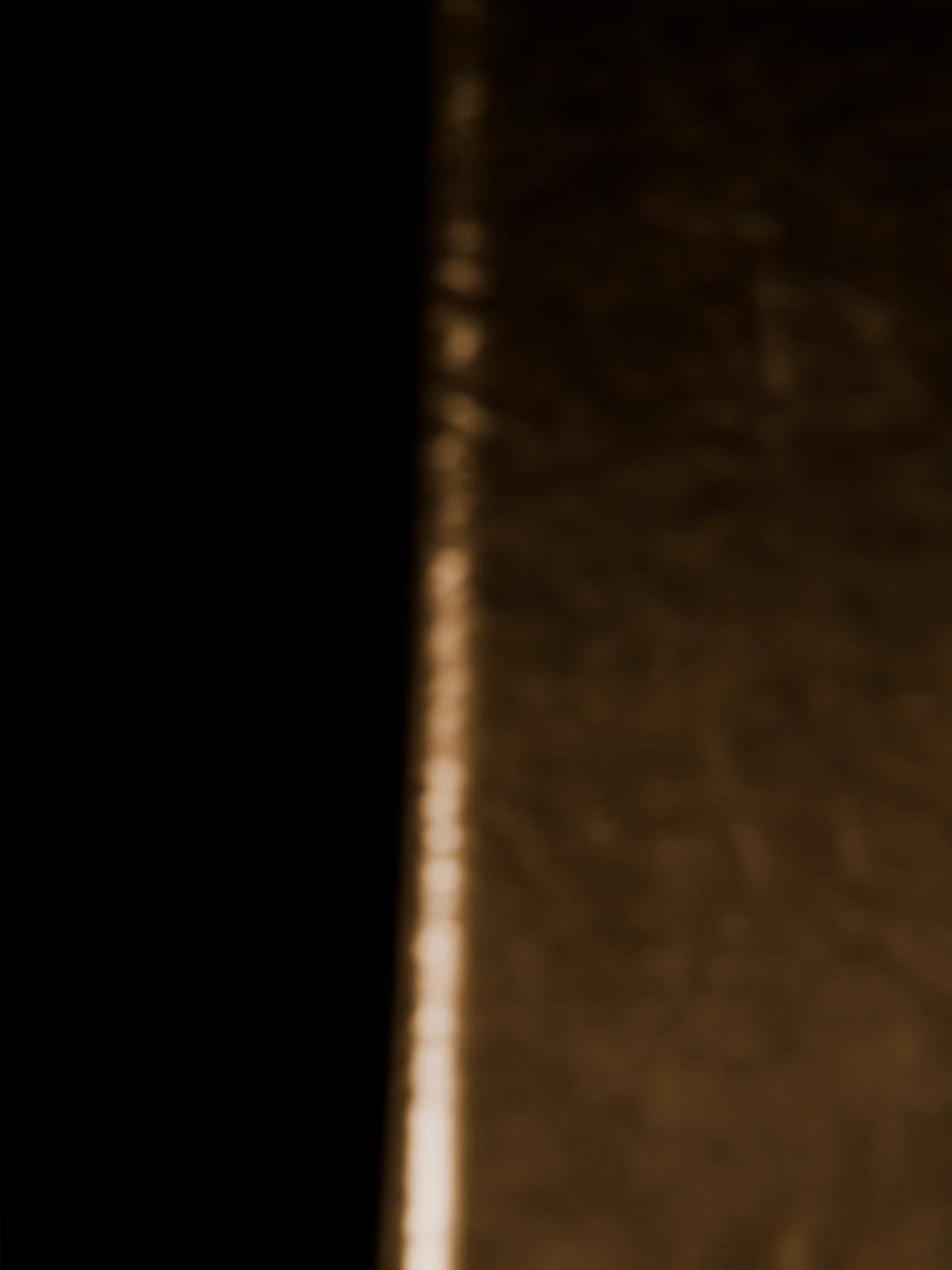 Close-up of a textured surface with light reflection creating a vertical bright line on the right side against a dark background on the left.