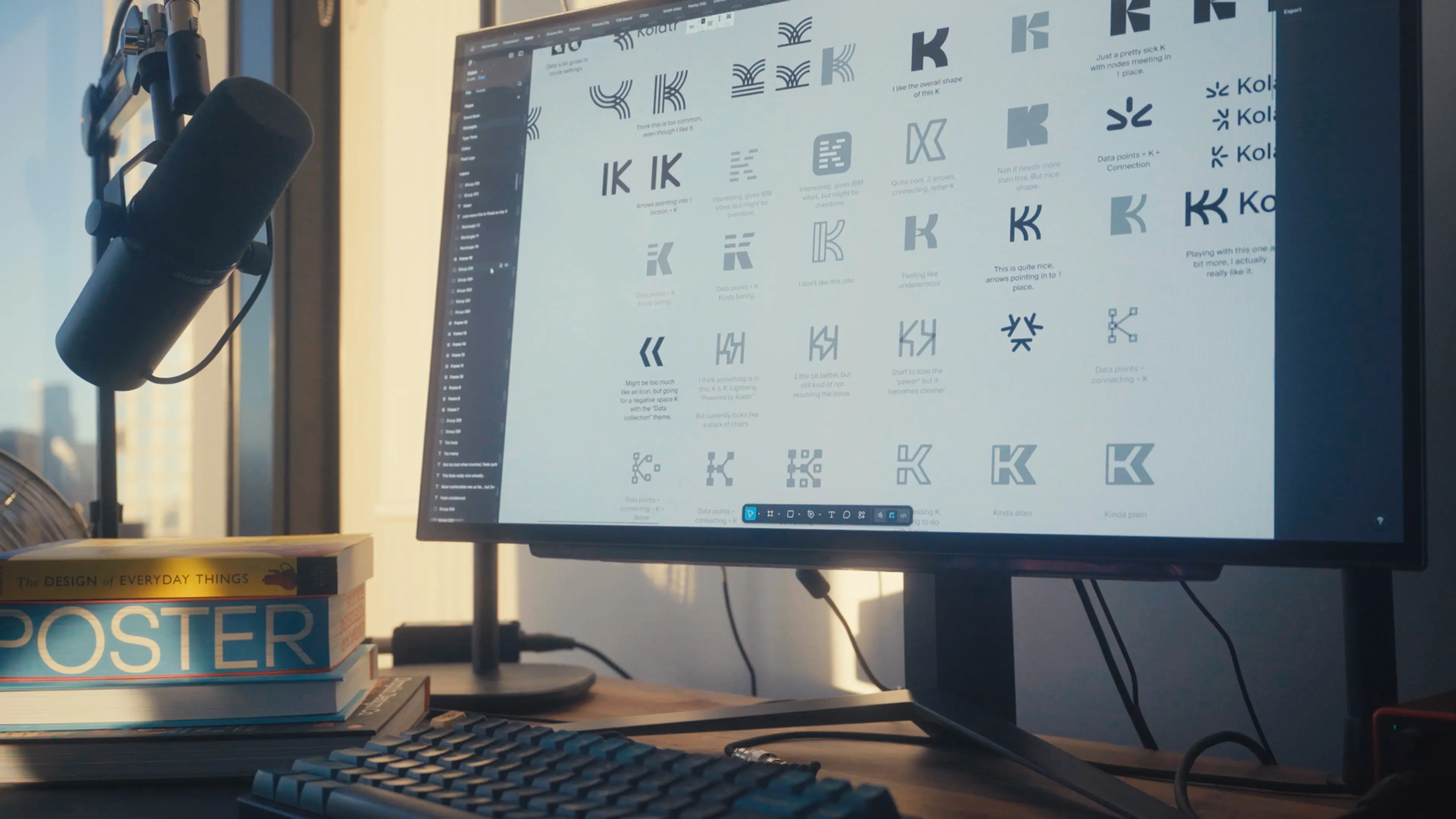 Desk setup with a black microphone, stacked design books including 'Poster' and 'The Design of Everyday Things,' a keyboard, and a monitor displaying various logo designs.