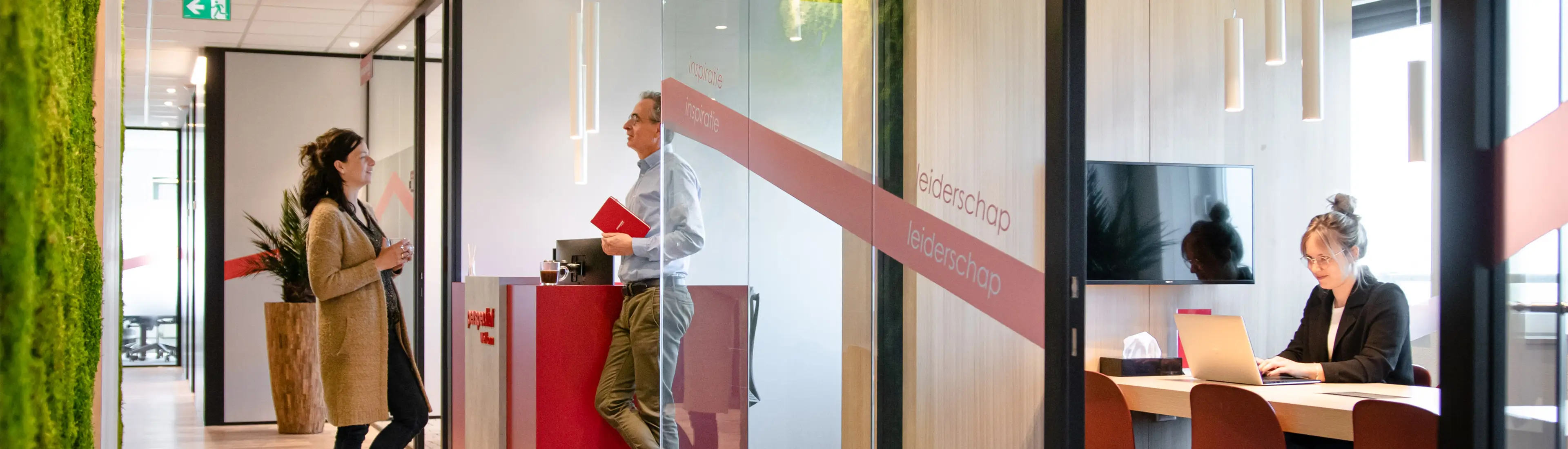 Kantoor Perspectief met werkende vrouw achter laptop aan bureau en staand gesprek op de gang tussen man en vrouw