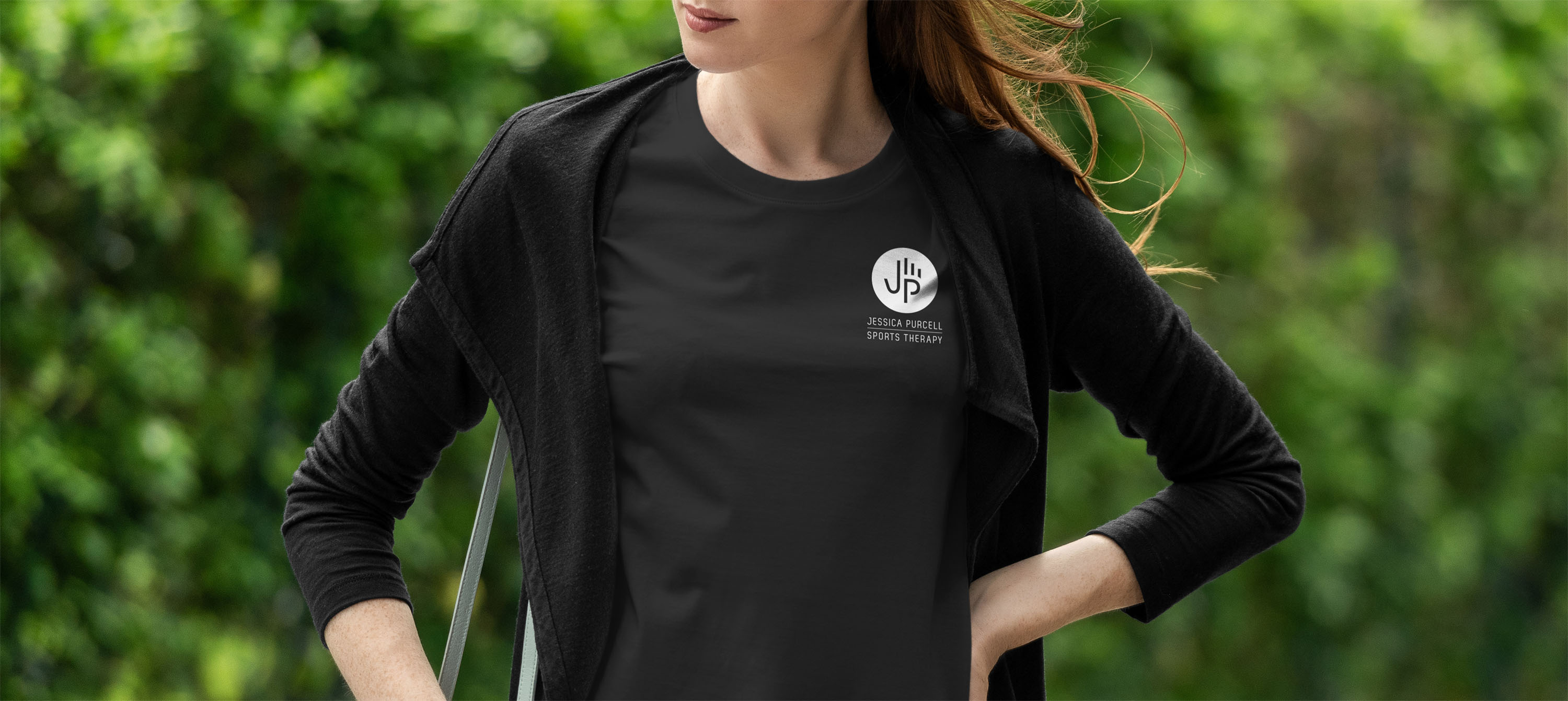 White Jessica Purcell Sports Therapy abstract hand logo on a black T-shirt worn by a woman.