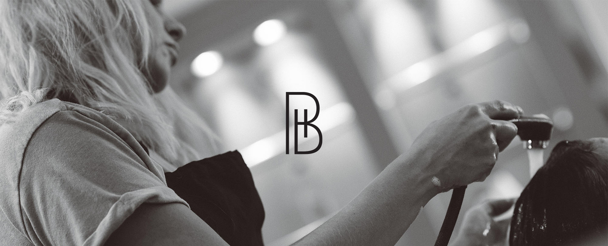 Monogram BH logo overlaid on a black and white photo of a woman washing hair in a salon.