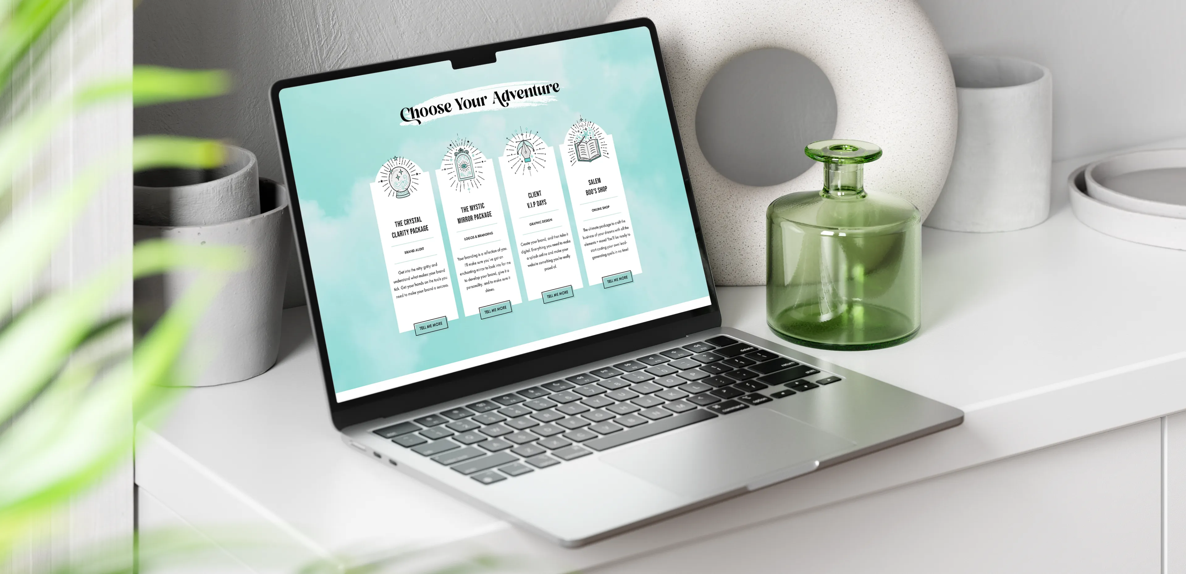 MacBook on a sideboard displaying four hand-drawn icons on Infinity Creative’s website, including a crystal ball, mystic mirror, and spell book.
