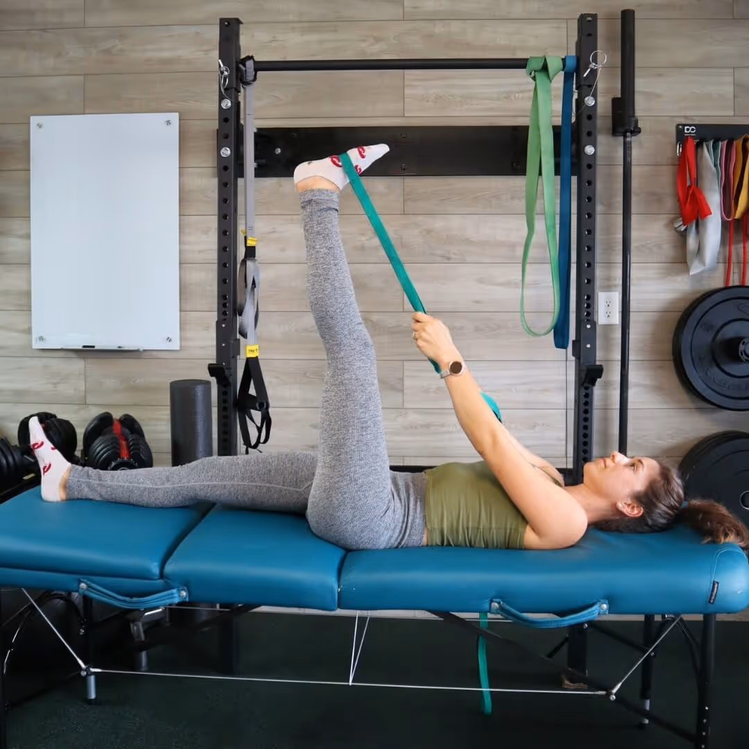A girl lying on her back stretching her leg upwards with a strap