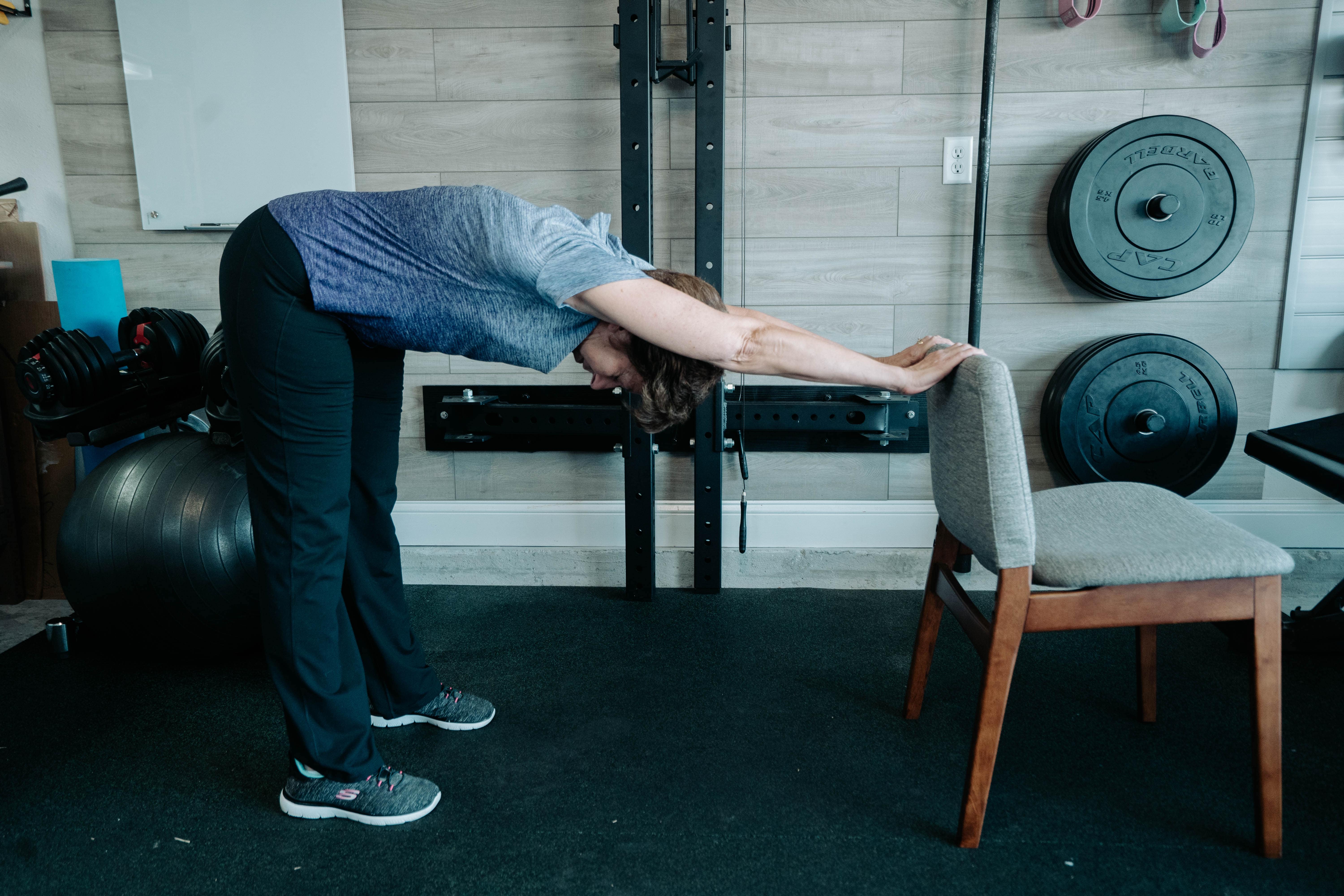 Older lady holding onto a chair demonstrating the standing L stretch