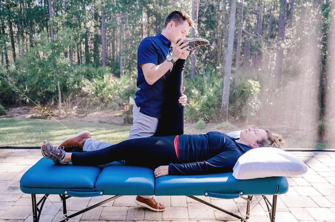 Dr. Michael Derry guiding a patient through a supported leg stretch on a treatment table at their home