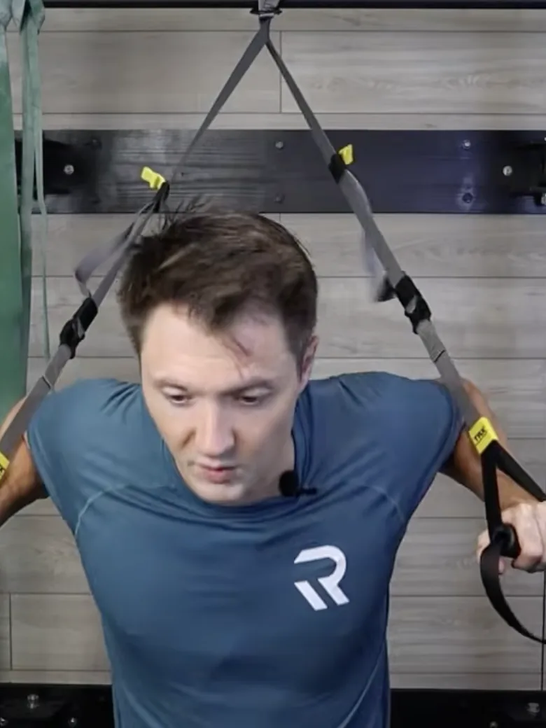 Dr. Michael Derry demonstrating a suspension trainer chest press, leaning forward into the straps