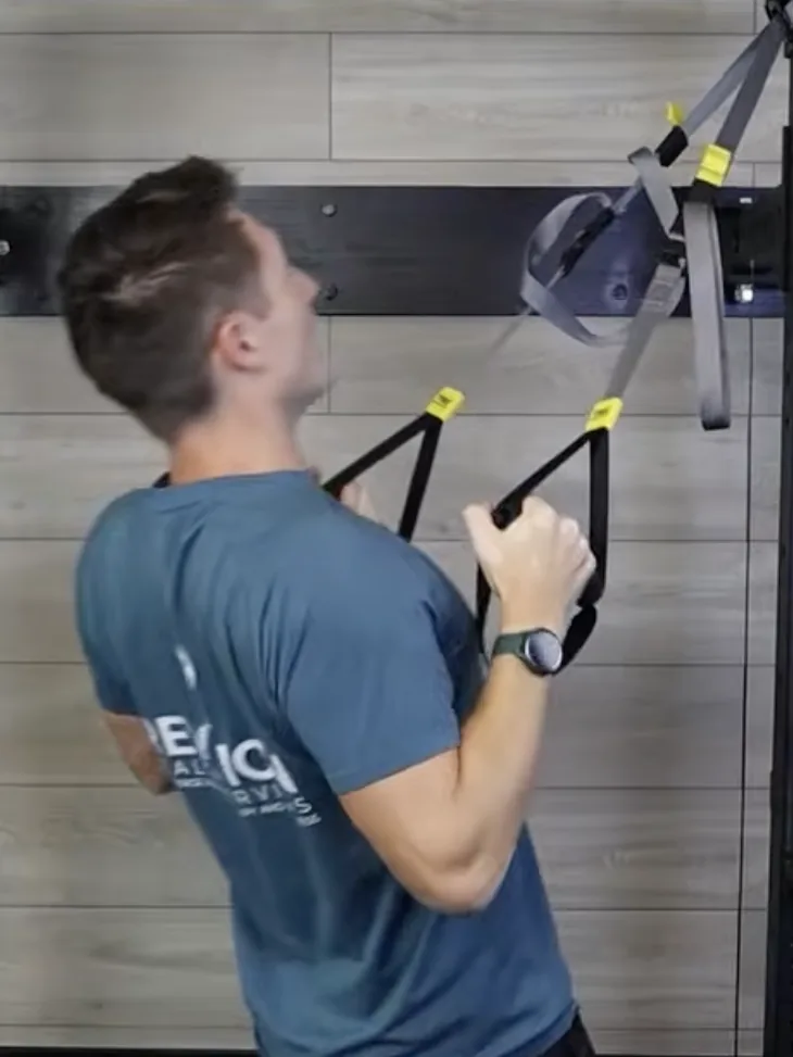 Dr. Michael Derry demonstrating a suspension trainer row, leaning back and pulling the handles toward his chest
