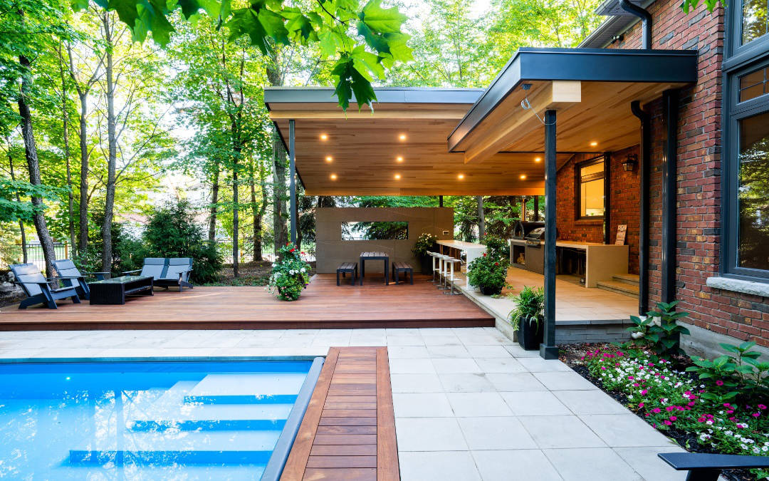 An open and partially covered extended patio with large trees and small flowers near an outdoor pool.