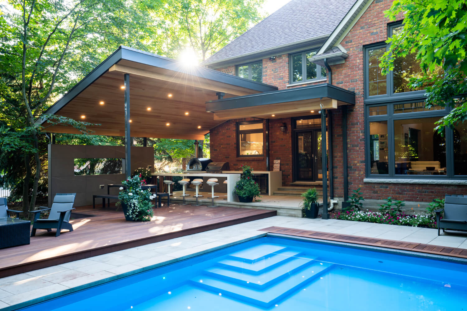 A pool near a stone patio and a covered outdoor dinning and living area.