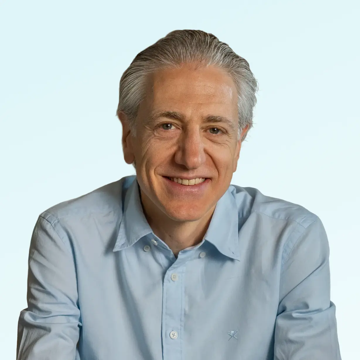 Smiling middle-aged man with gray hair wearing a light blue button-up shirt against a plain background.