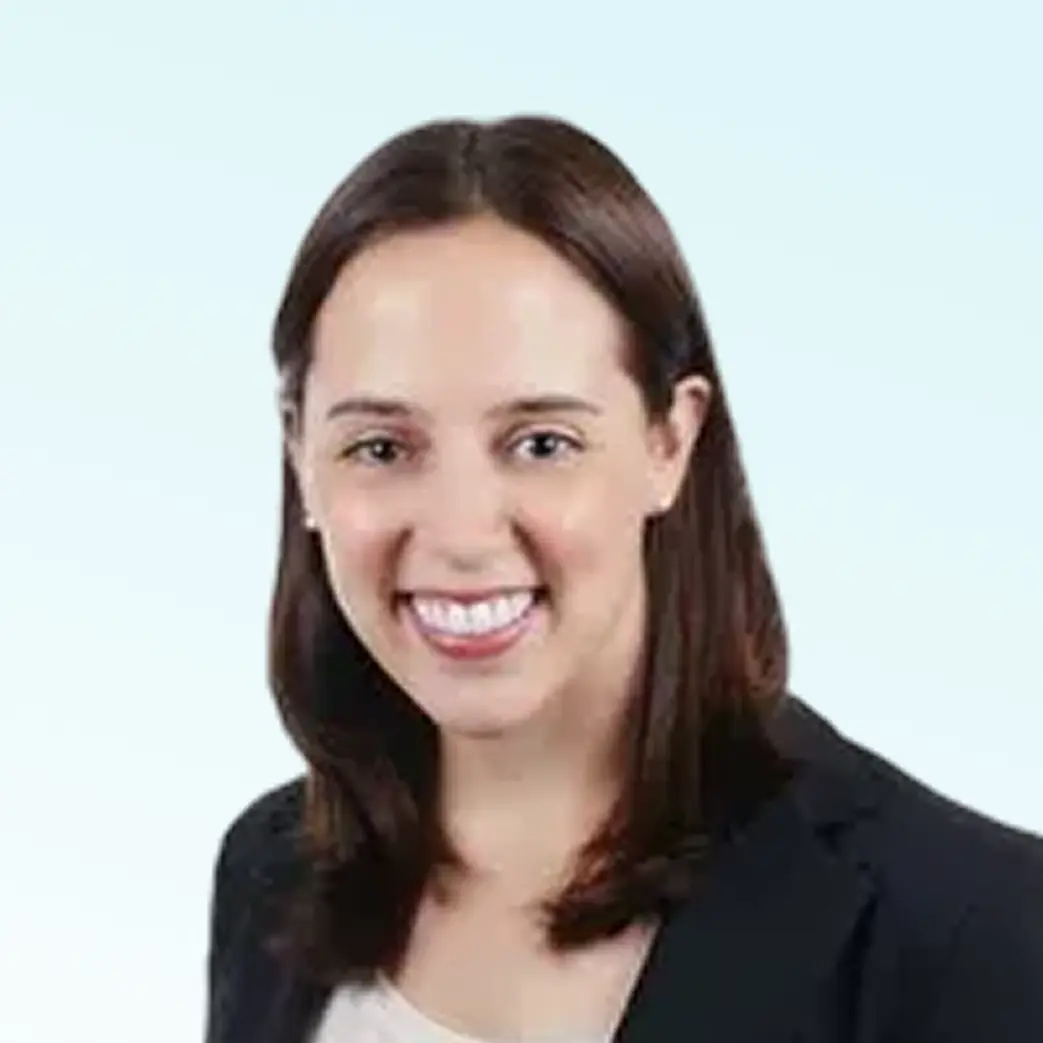 Smiling woman with shoulder-length brown hair wearing a black blazer and light-colored top against a light background.