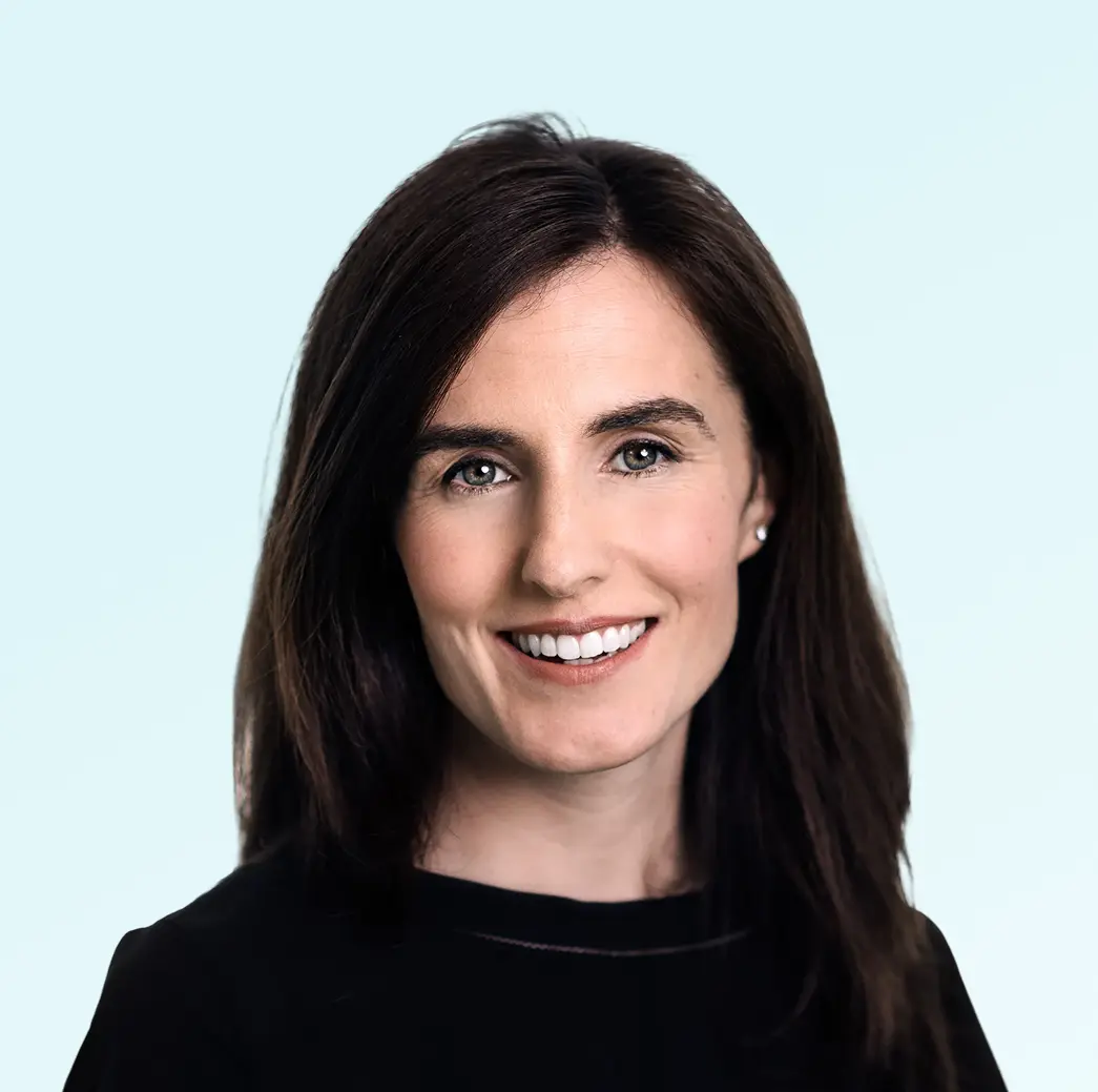 Smiling woman with straight dark brown hair wearing a black top against a light blue background.