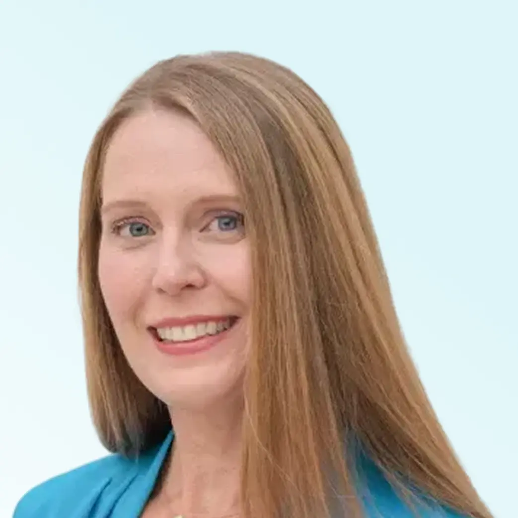 Smiling woman with long straight blonde hair wearing a blue top and a small necklace.