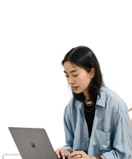 Young woman with black hair focused on typing on a laptop while seated.