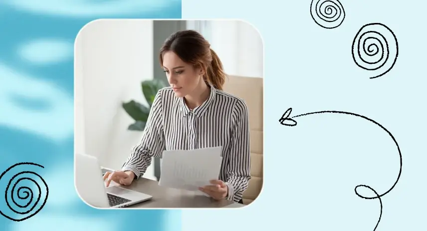 Woman in striped shirt looking at laptop screen while holding documents at a desk.