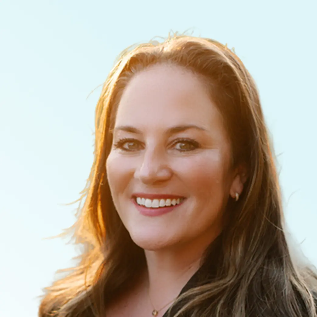 Smiling woman with long brown hair and light makeup against a light background.