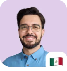 Smiling man with beard and glasses wearing a blue collared shirt against a light purple background, with a small Mexican flag icon at the bottom right corner.