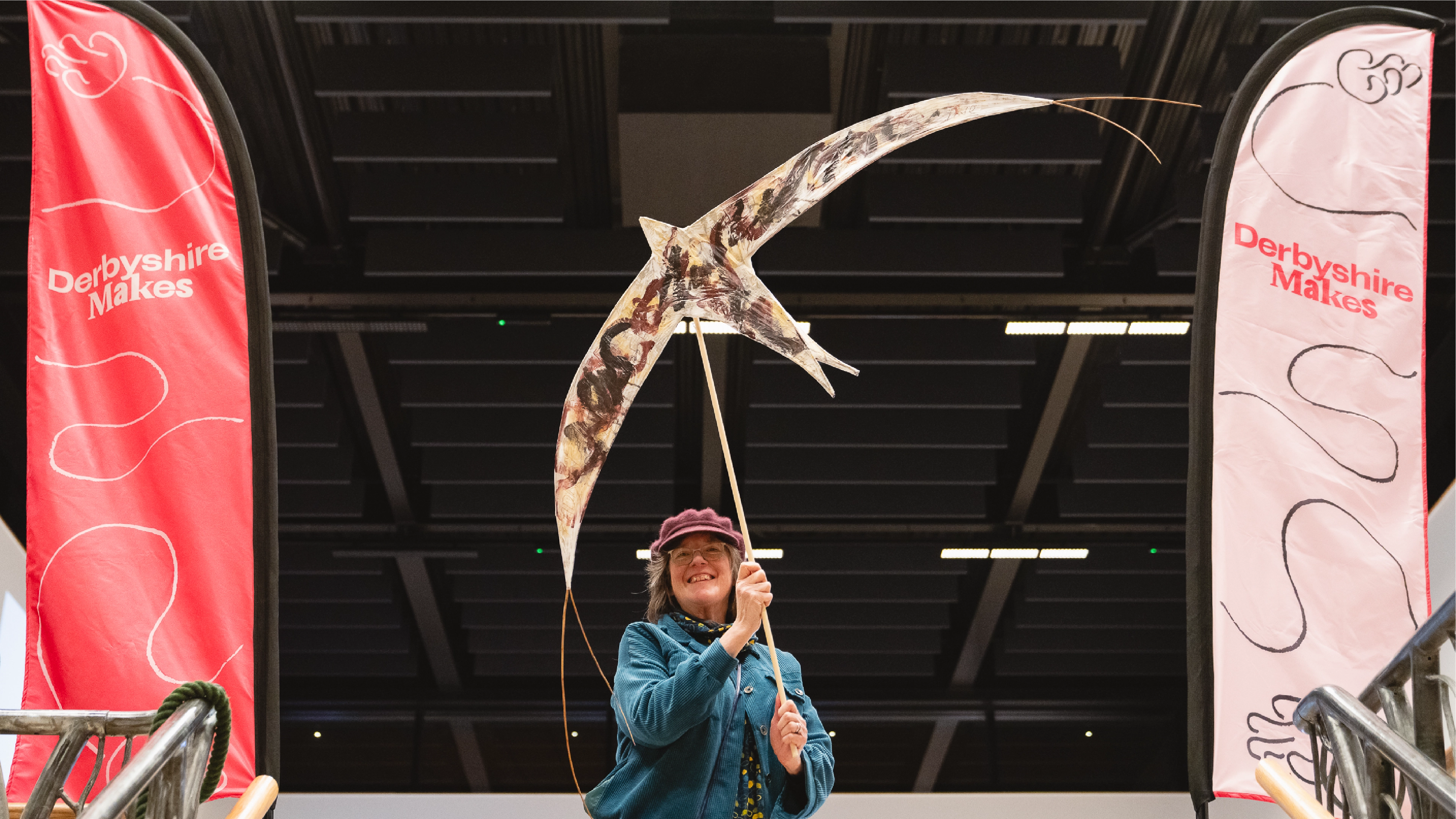 Lady with a swift puppet at the Derbyshire Makes launch next to 2 flags, one red and one pink with the brand identity created by Sanna Studio