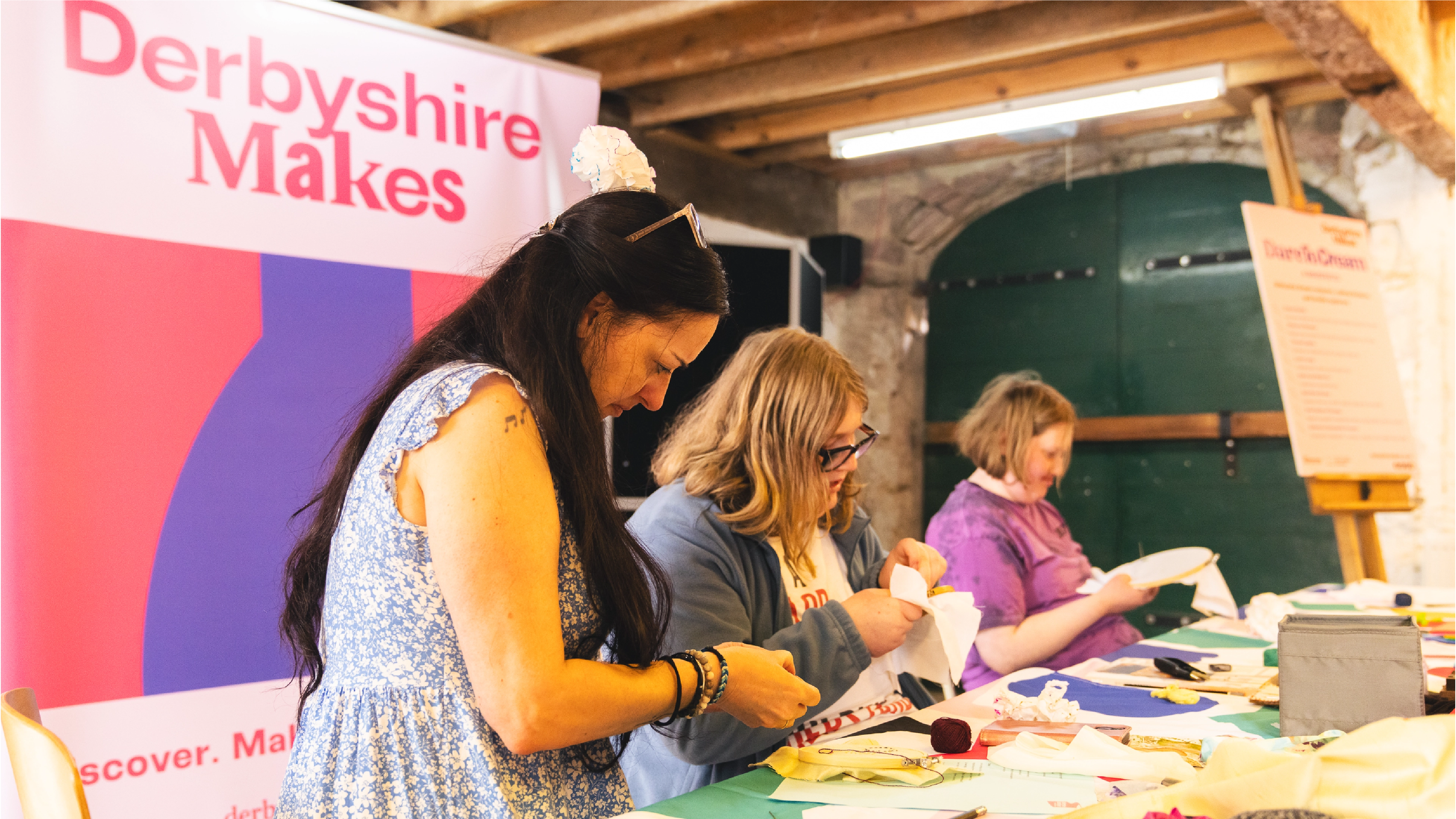 People making crafts at Derbyshire Makes festival in front of a banner with the branding created by Sanna Studio