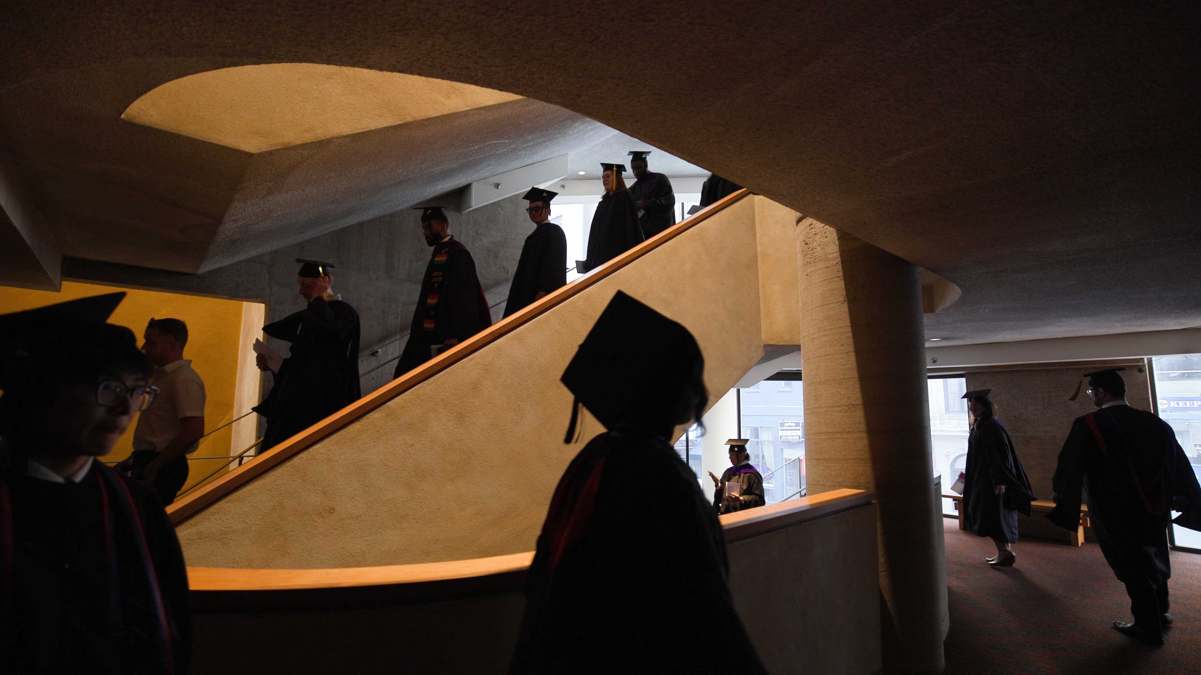Silhouette of Penn Carey Law graduates walking down a spiral staircase during commencement.