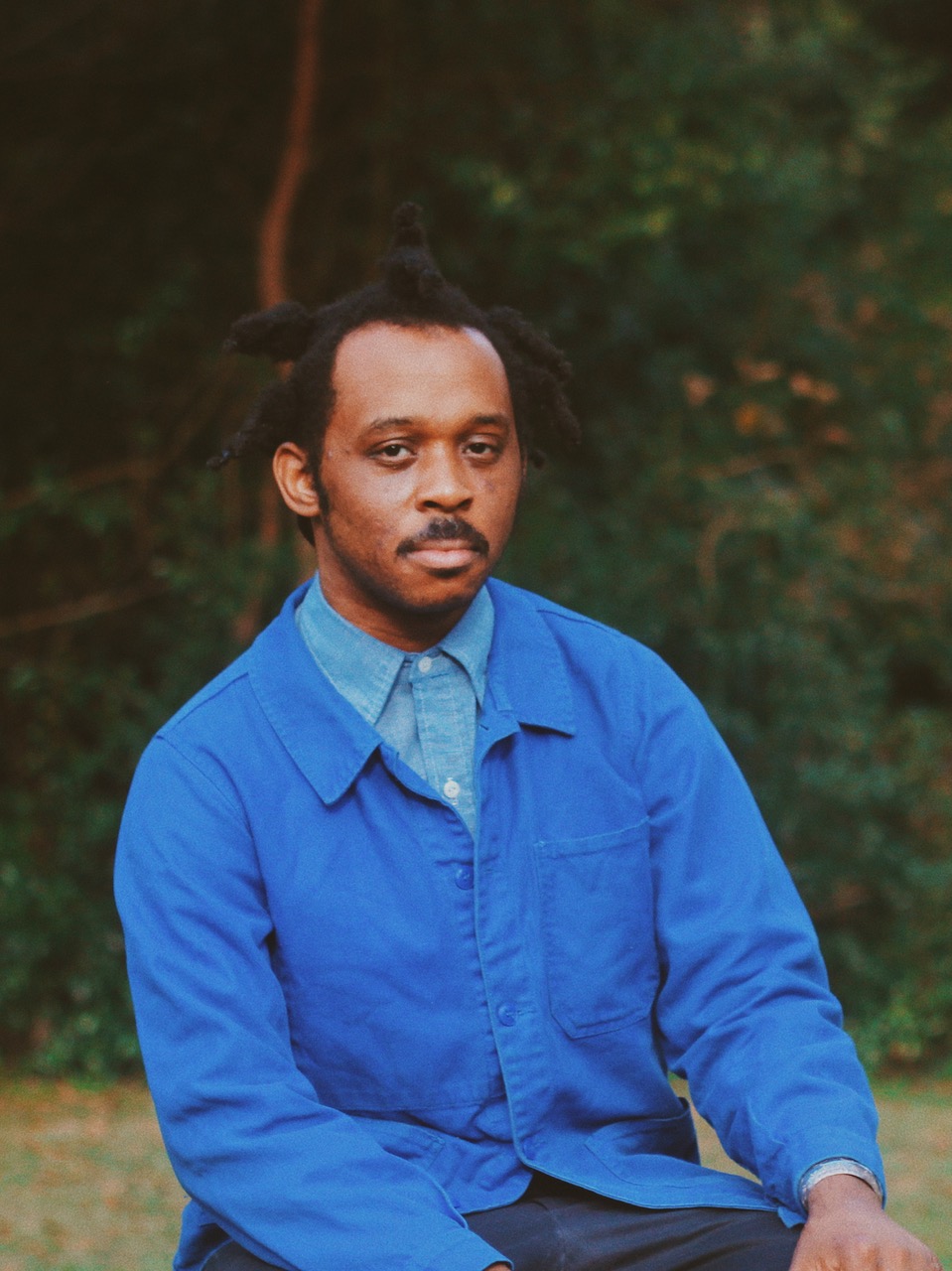 Headshot of Curry Hackett sitting in front woods with indigo blue jacket and denim shirt.