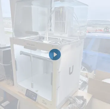 Imprimante 3D Ubiquiti sur une table près d'une fenêtre avec un véhicule visible à l'extérieur.