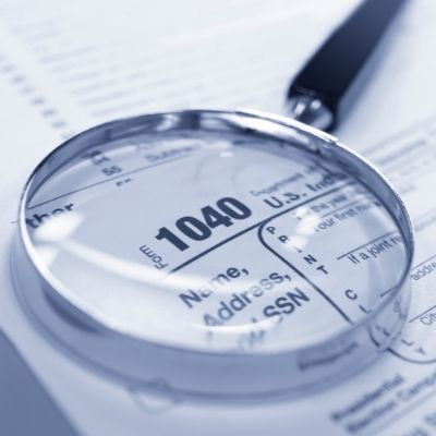 Magnifying glass examining a Form 1040 during a tax audit