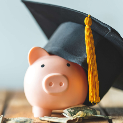 Piggy bank wearing a graduation cap beside dollar bills