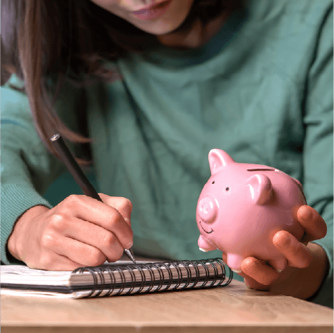 woman writing in a budget planner holding a piggy bank