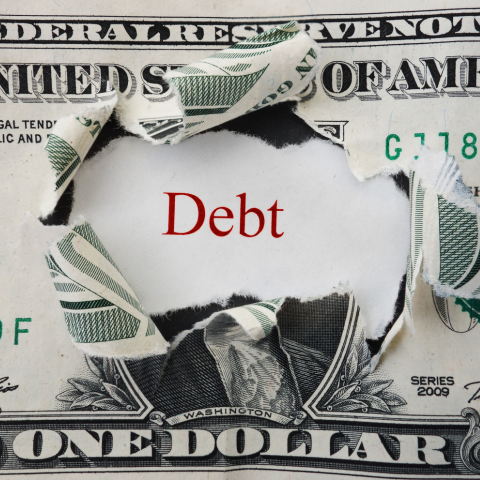 the word debt behind a dollar bill