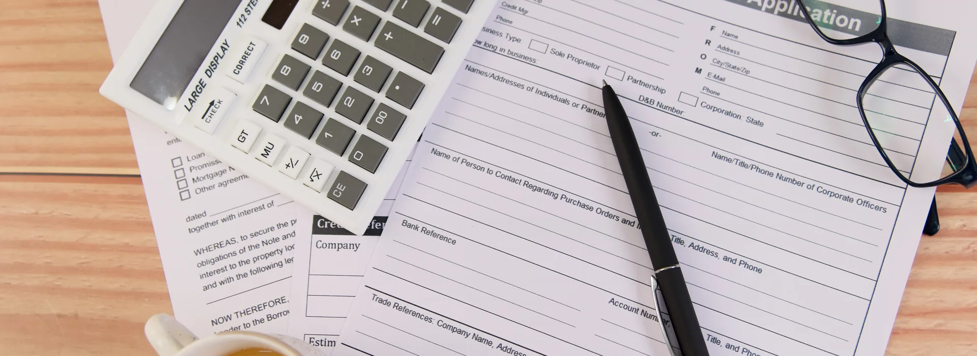 Loan application paperwork with a calculator, pen, and glasses